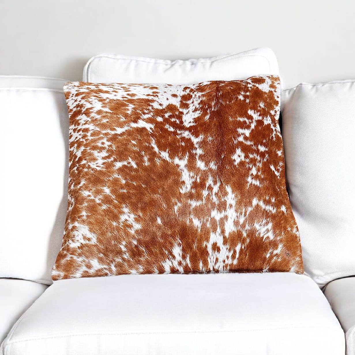 Brown and white cowhide patterned pillow on a white sofa