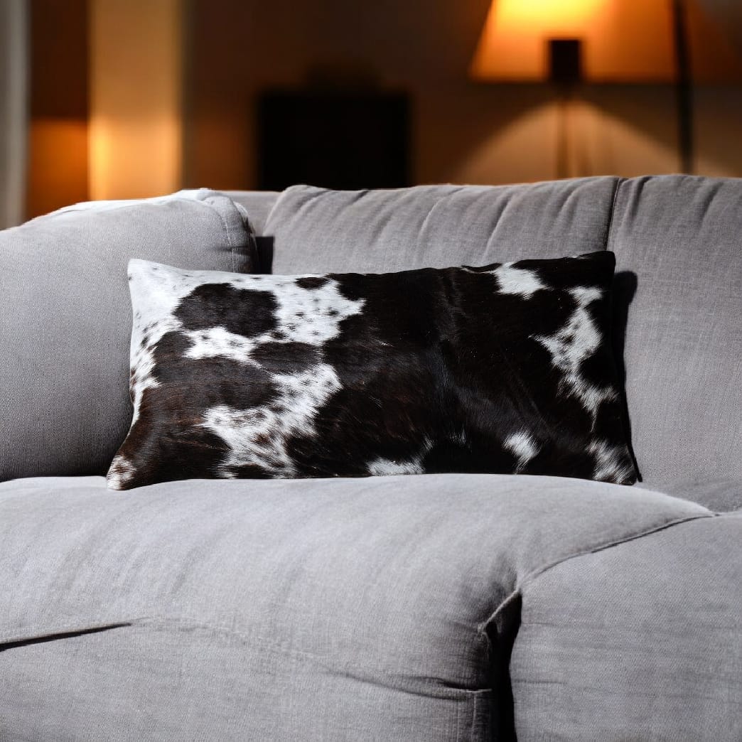 Gray sofa with a black and white cow print pillow in a cozy living room setting.
