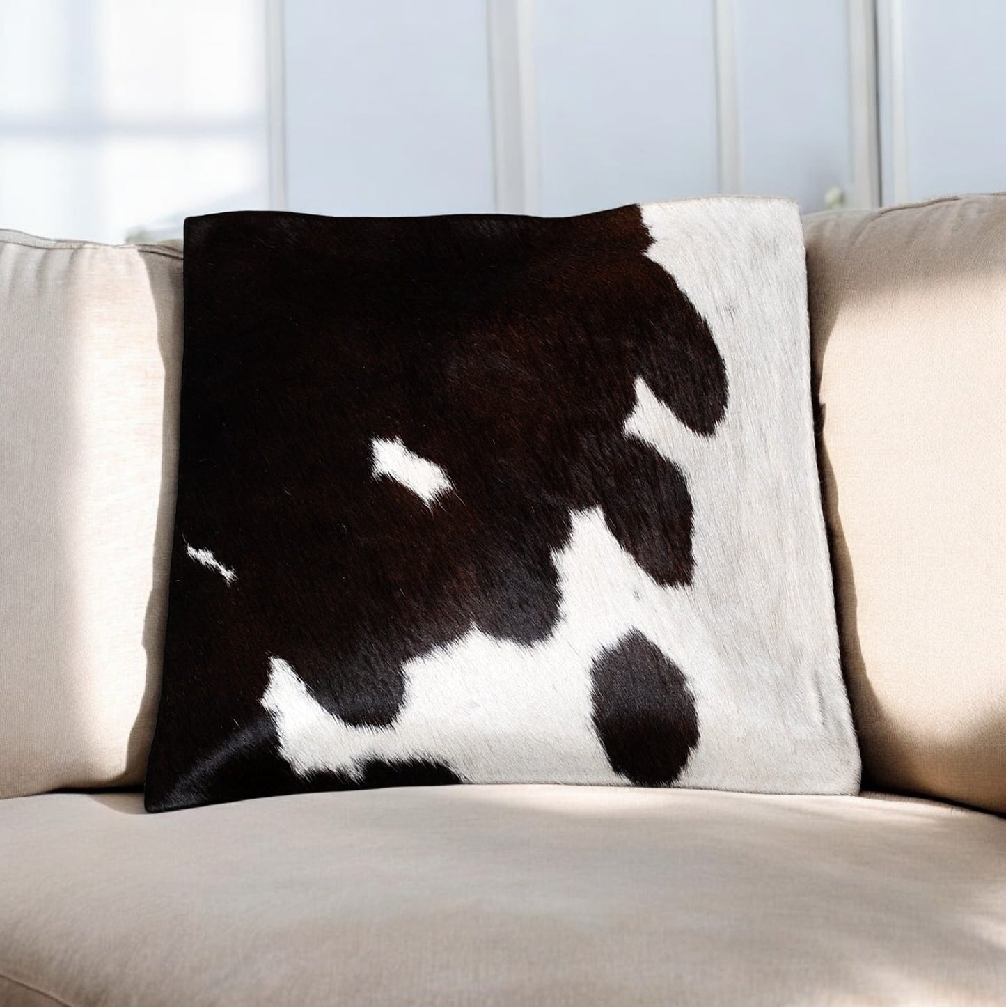 Cow print pillow on a beige sofa with a white wall background