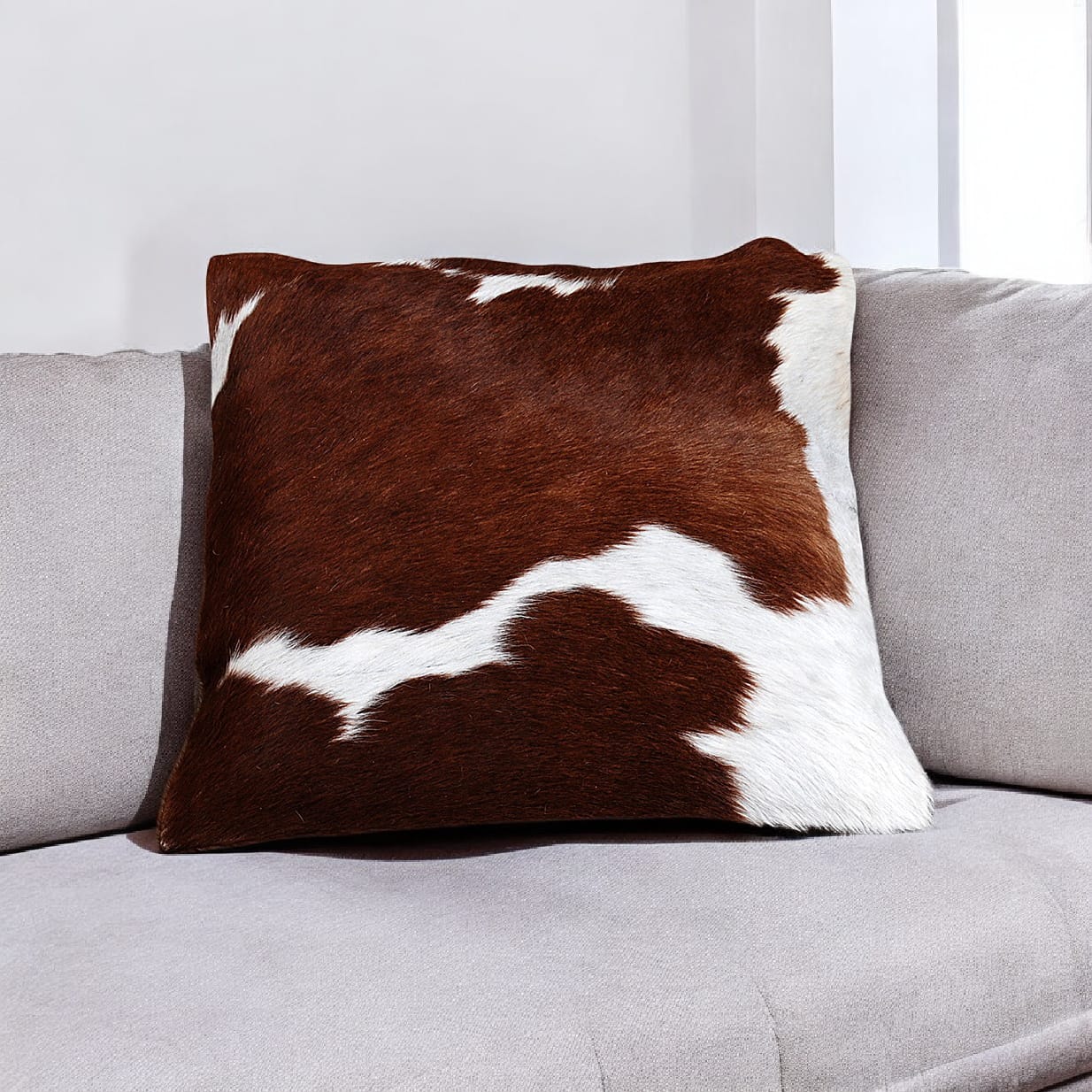 Brown and white cowhide pillow on a gray sofa