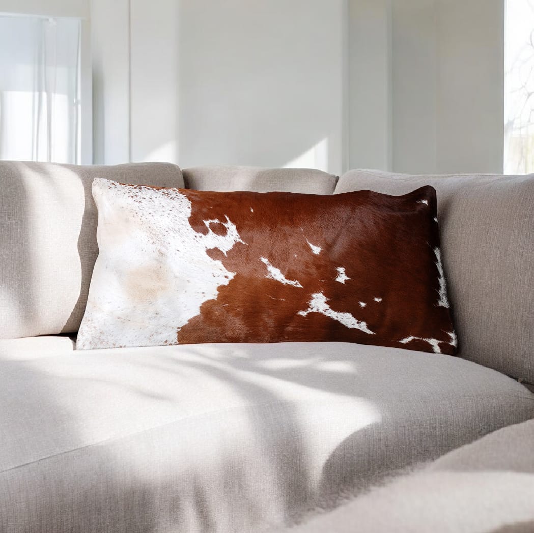 Brown and white cowhide pillow on a gray sofa with a neutral background