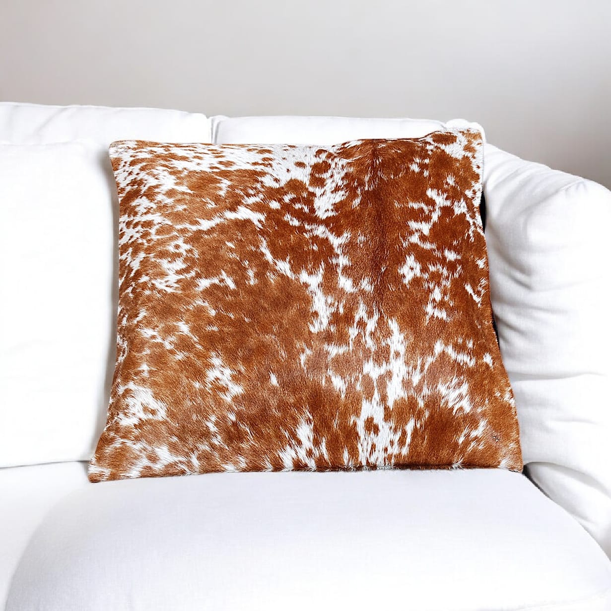 Brown and white cowhide patterned pillow on a white sofa