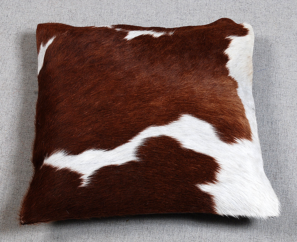 Brown and white cowhide pillow on a gray background