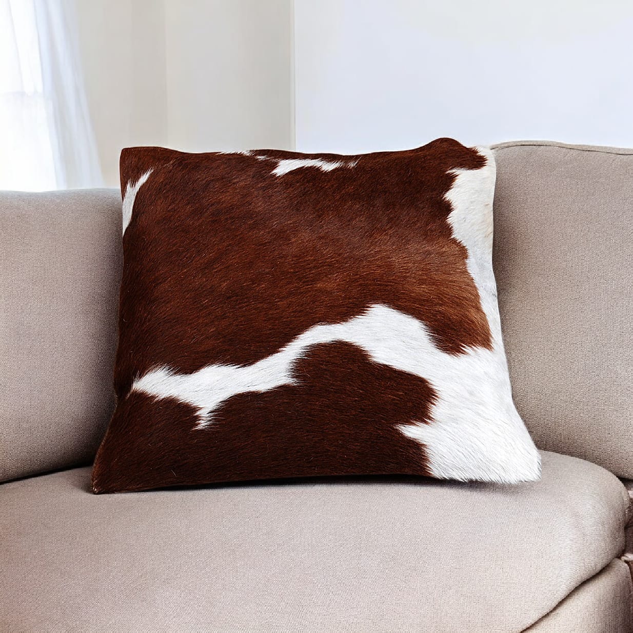 Brown and white cowhide pillow on a beige sofa